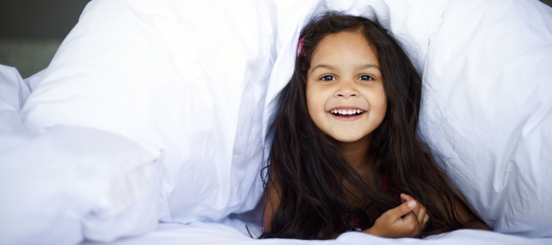 Happy young girl with long hair smiling under a cozy white blanket