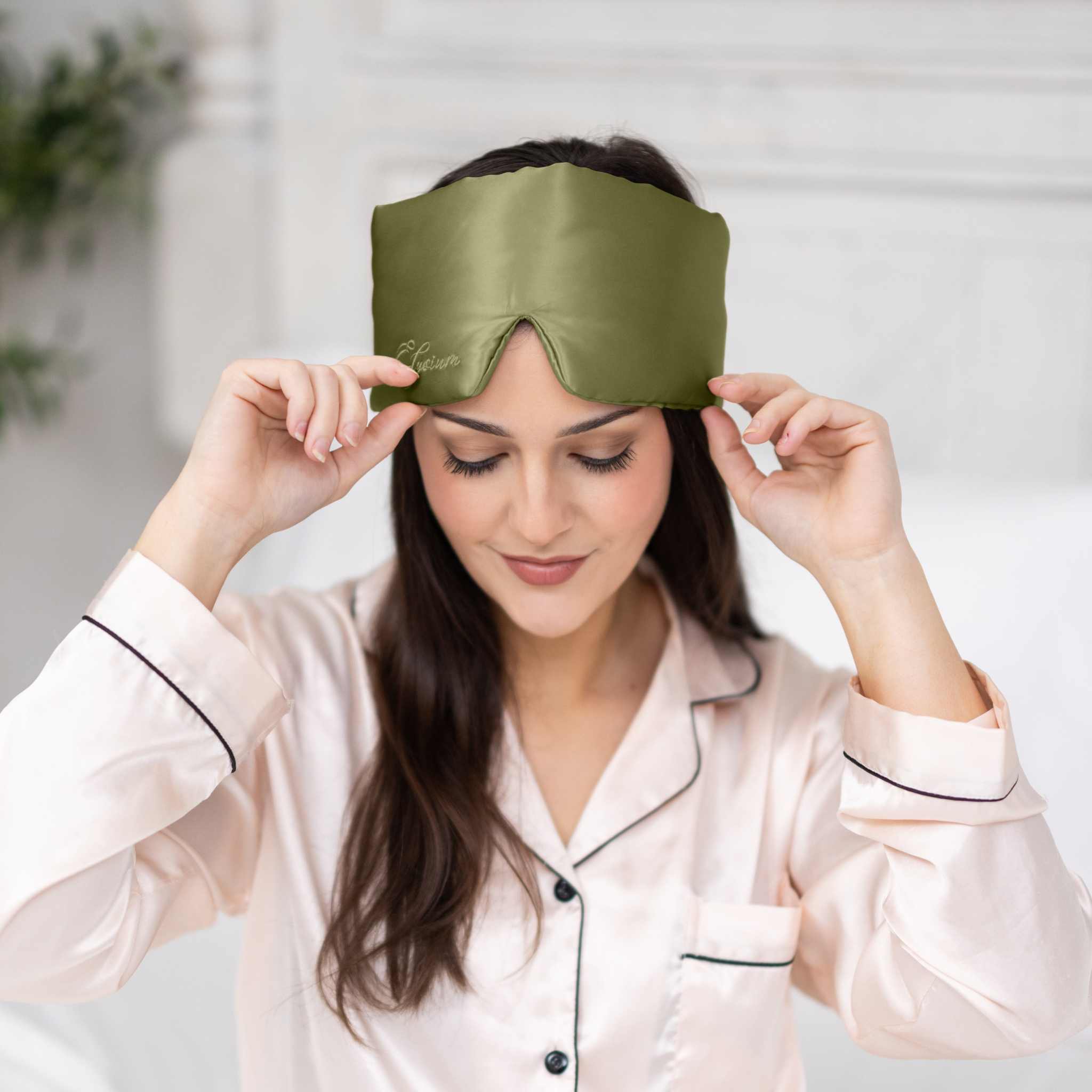 Woman putting on Elysium Silk Sleep Mask in Avocado