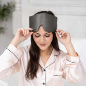 Young woman sitting in bed with Elysium Silk Sleep Blindfold in Metal Grey