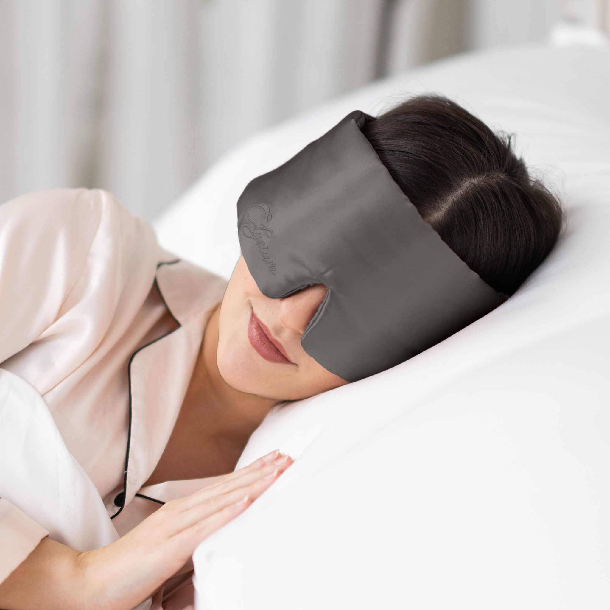 Young woman side sleeping in bed with Elysium Silk Sleep Blindfold in Metal Grey