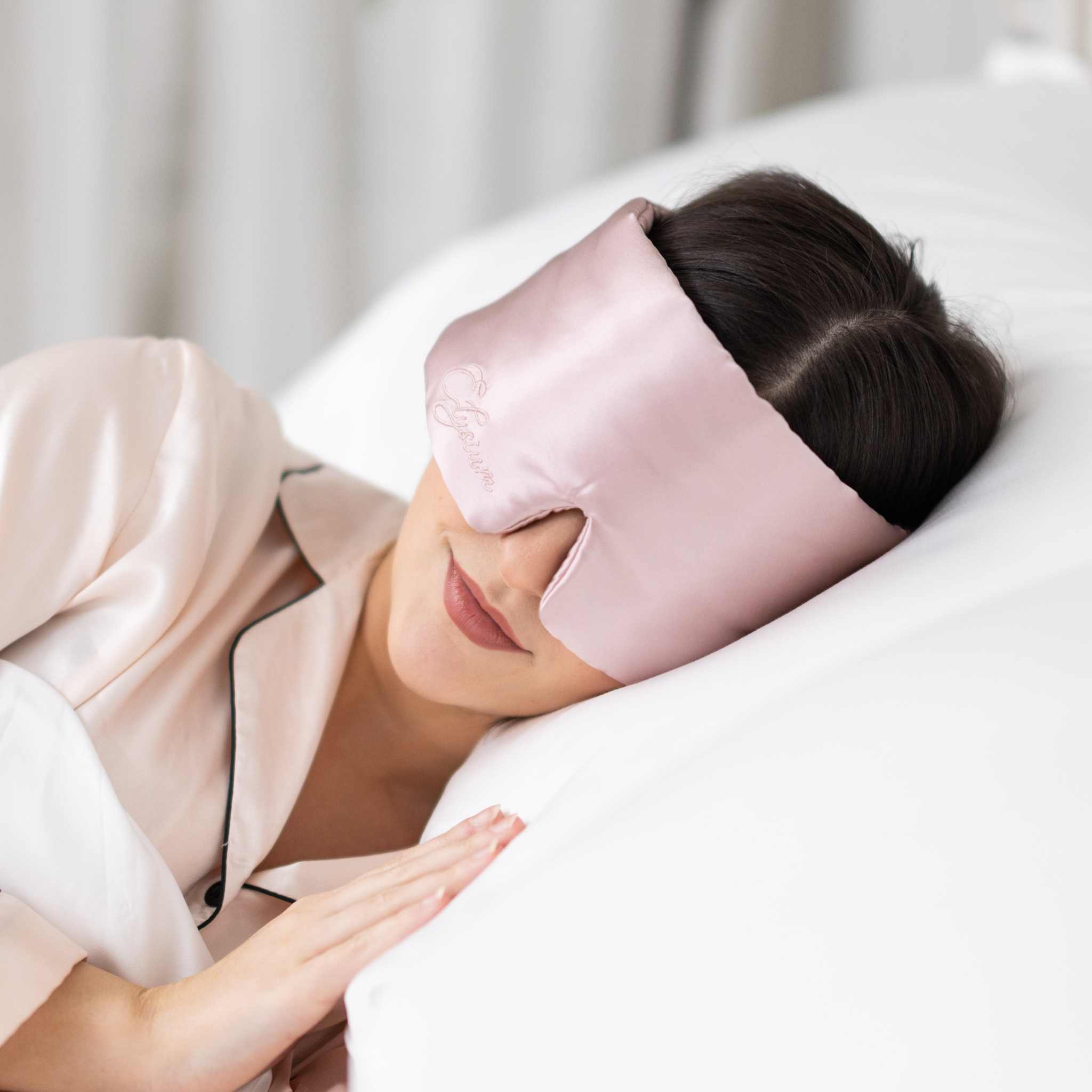 Woman resting in bed with Elysium Silk Eye Mask for eyes in Pink