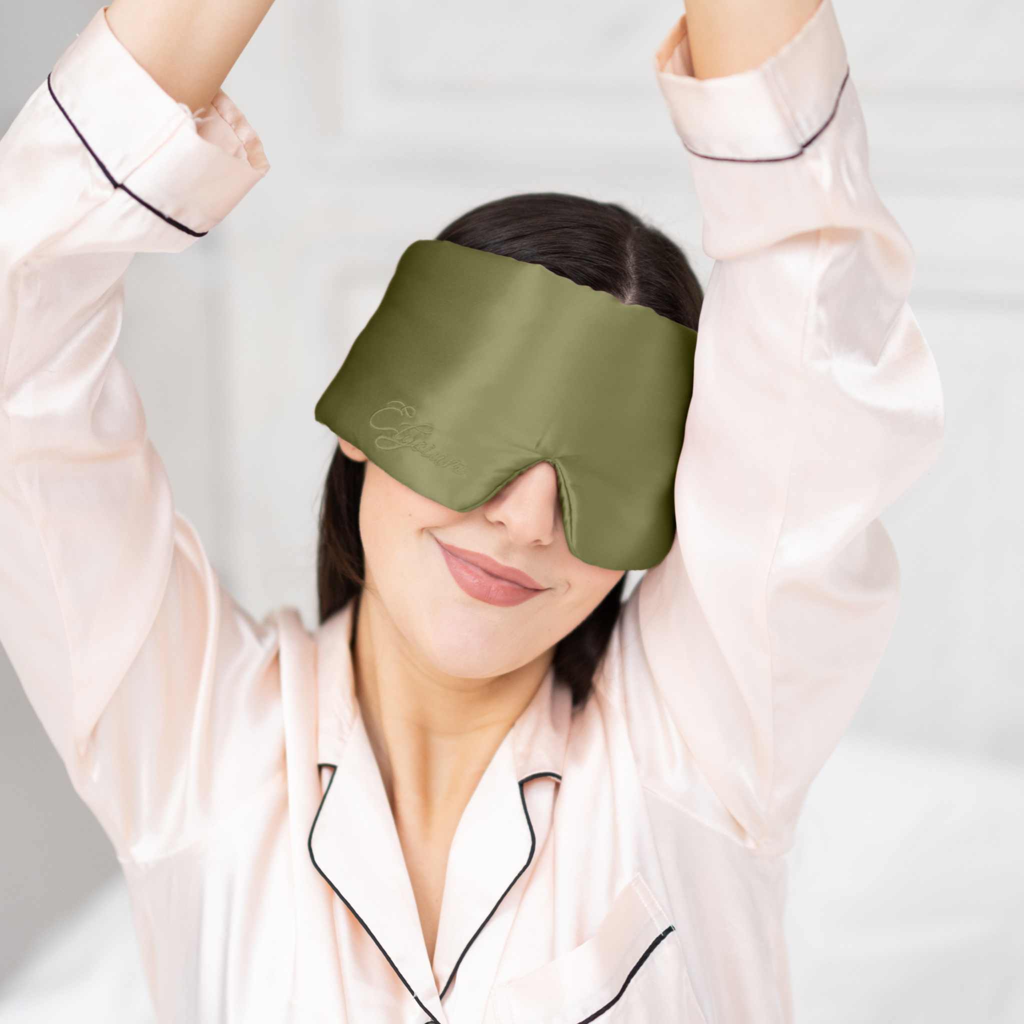 Young woman waking up in bed with Elysium Silk Sleep Mask in Avocado