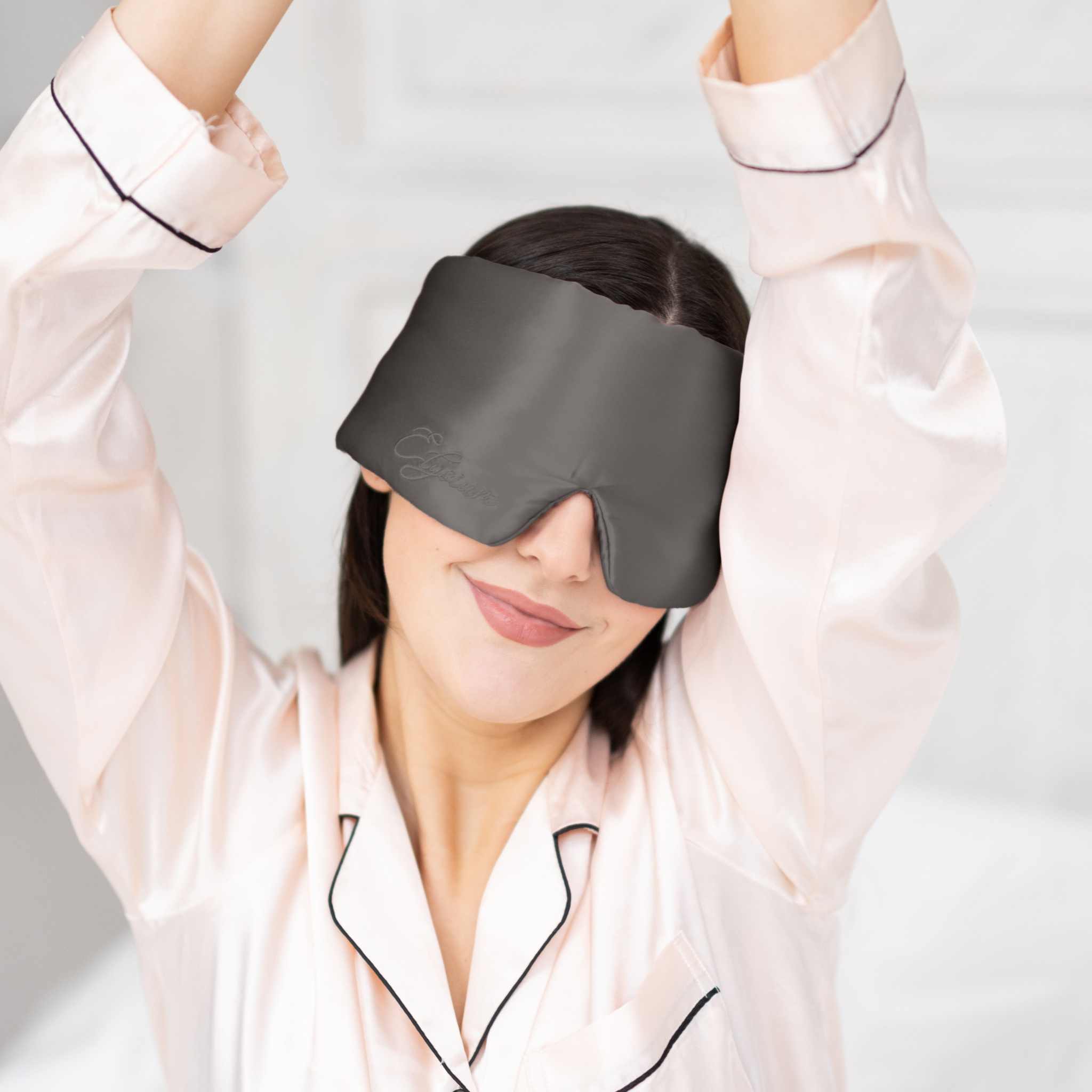 Young woman waking up in bed with Elysium Silk Sleep Blindfold in Metal Grey