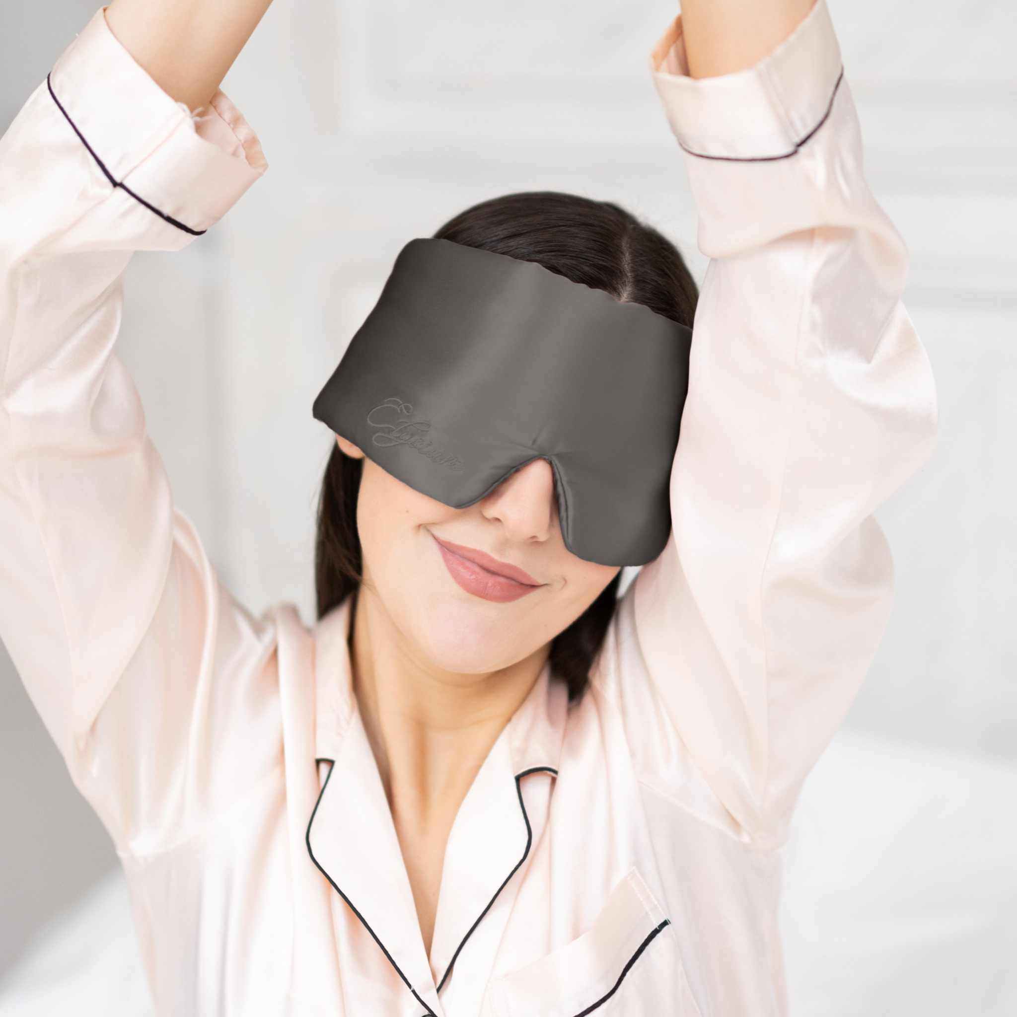 Young woman waking up in bed with Elysium Silk Sleep Blindfold in Metal Grey