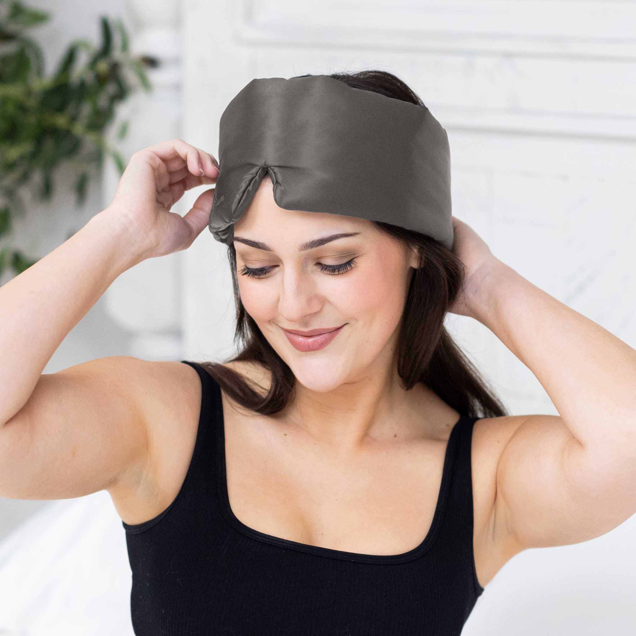 Woman putting on Elysium Silk Sleep Blindfold in Metal Grey