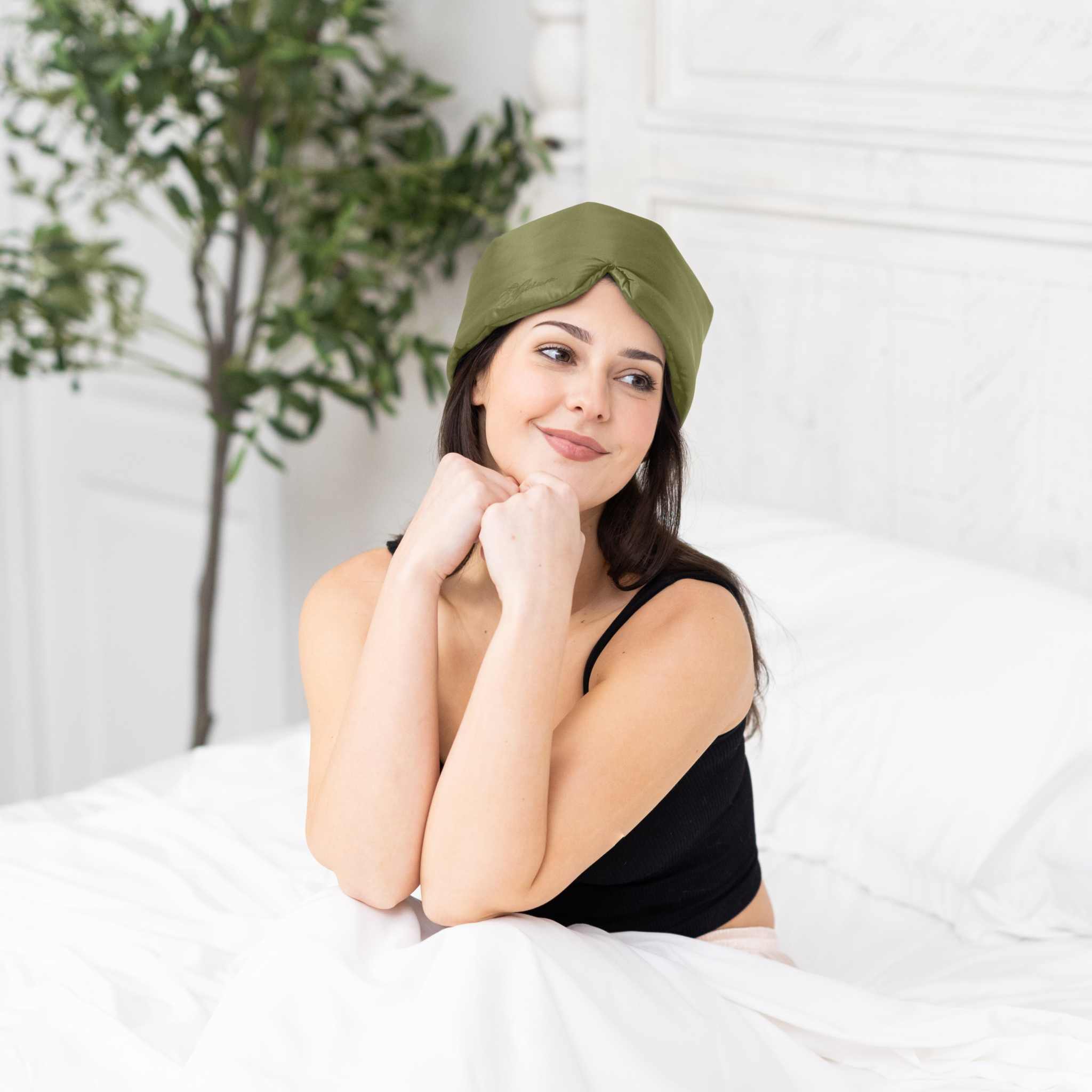 Young woman sitting in bed with Elysium Silk Sleep Mask in Avocado