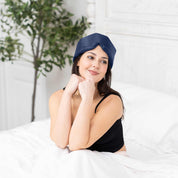 Young woman sitting in bed with Elysium Silk Eye Mask in Navy 