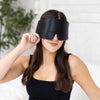 Woman adjusting an Elysium Silk Eye Mask for sleeping in Black